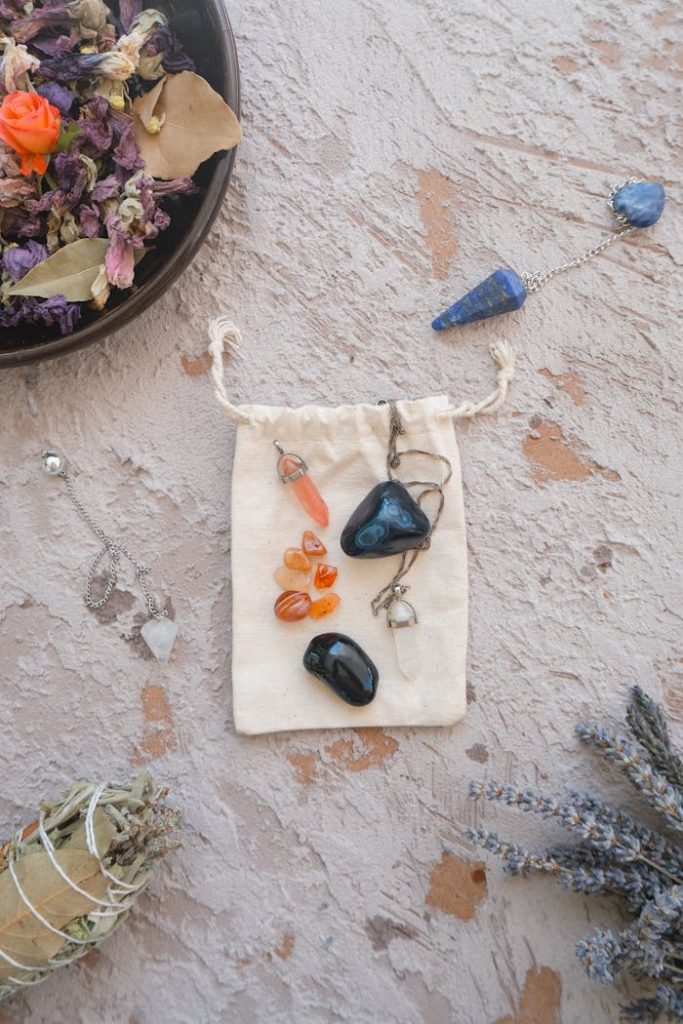 Flat lay of healing crystals, dried flowers, and pendulums for spiritual energy practices.