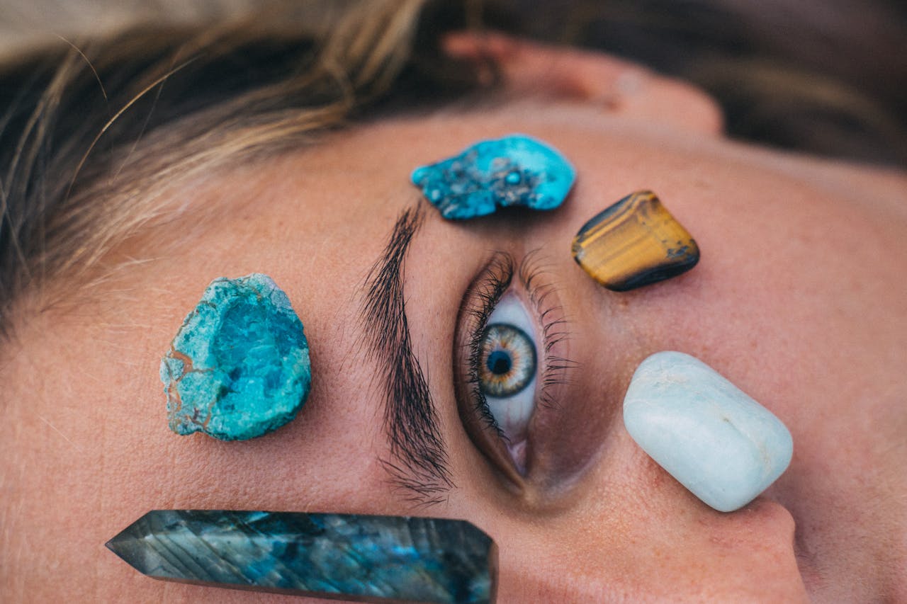 Close-up of a persons eye surrounded by vibrant healing stones on skin for relaxation therapy.